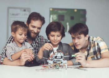 Two boys and male sit in the workshop and construct a robot.