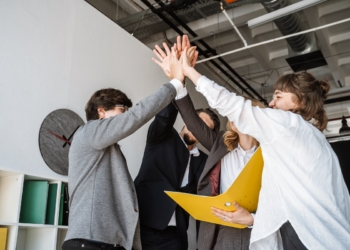 Cheerful young group of people standing in the office and giving high five while working together